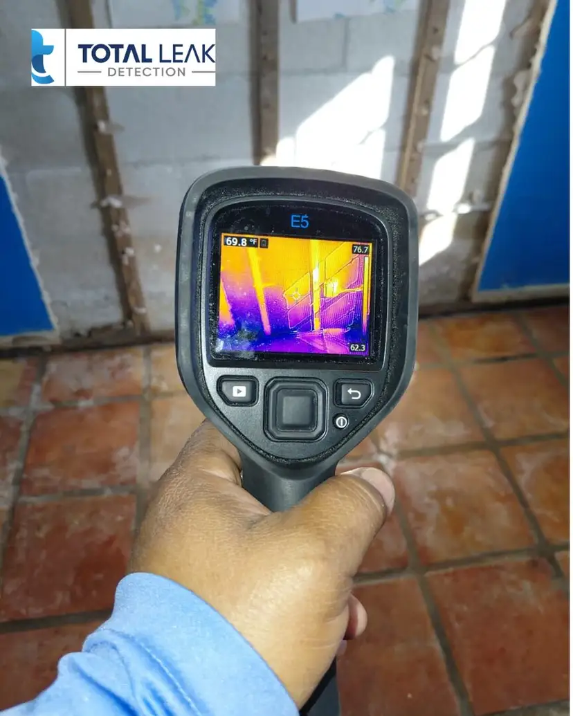 A thermal camera scans a tiled room where drywall has been removed to expose wall studs.